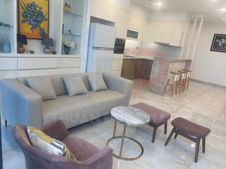 Phòng khách căn hộ hiện đại với sofa da màu be, bàn trà mặt đá tròn và bếp liền kề sáng màu