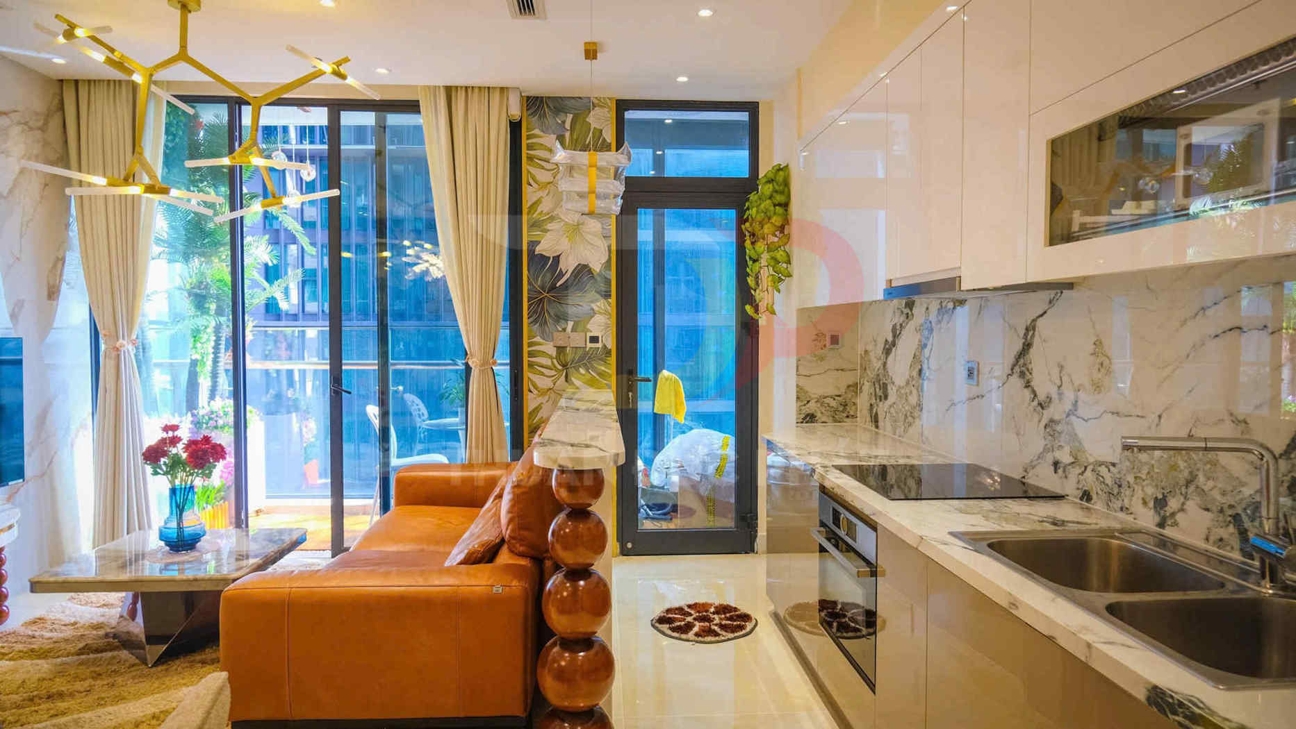 Phòng khách liền bếp hiện đại với sofa da nâu, tủ bếp đá marble và cửa kính lớn nhìn ra ban công
