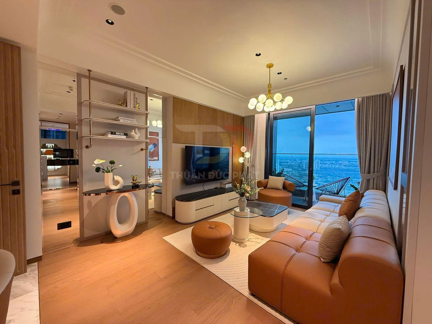 Phòng khách chung cư hiện đại với sofa da màu cam, bàn trà kính và cửa kính lớn nhìn ra ban công thành phố