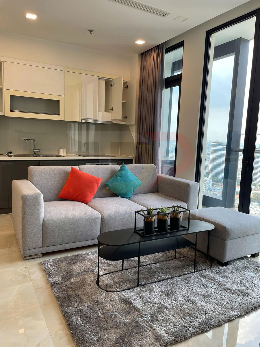 Sofa phòng khách màu xám với bàn trà đen, gối tựa nhiều màu và chậu cây nhỏ trong căn hộ hiện đại có cửa kính lớn