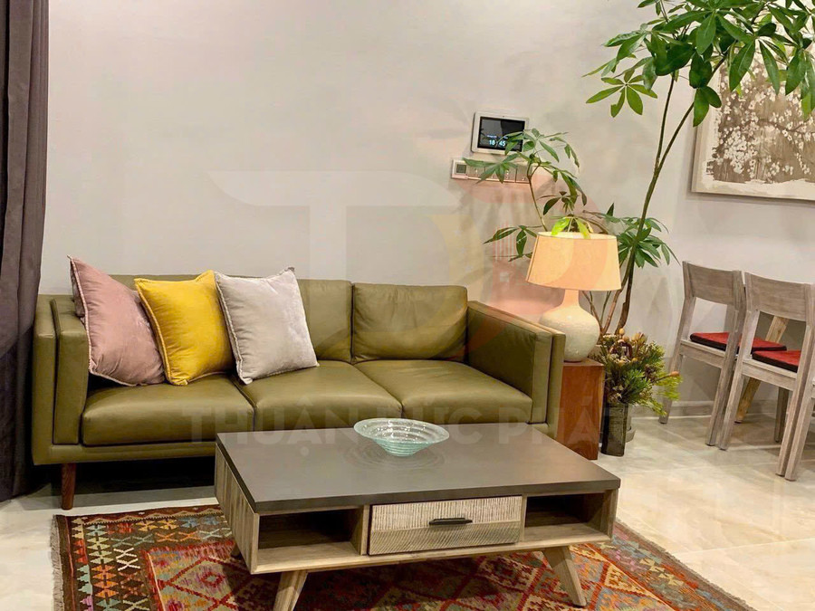 Sofa da màu xanh ô liu với gối tựa nhiều màu và bàn trà gỗ hiện đại trong phòng khách sáng sủa