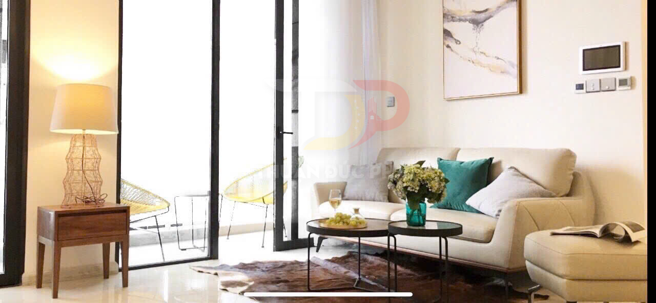 Phòng khách hiện đại với sofa da màu kem, bàn trà tròn và cửa kính lớn mở ra ban công sáng tự nhiên