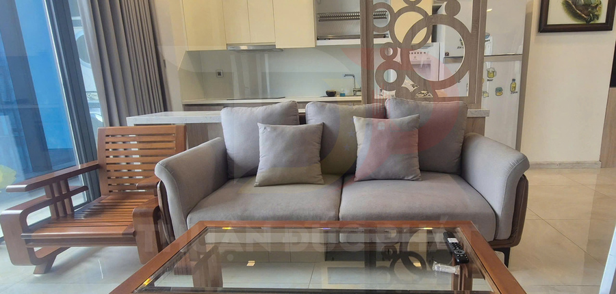 Sofa vải màu xám với ghế gỗ và bàn kính trong phòng khách cạnh bếp hiện đại