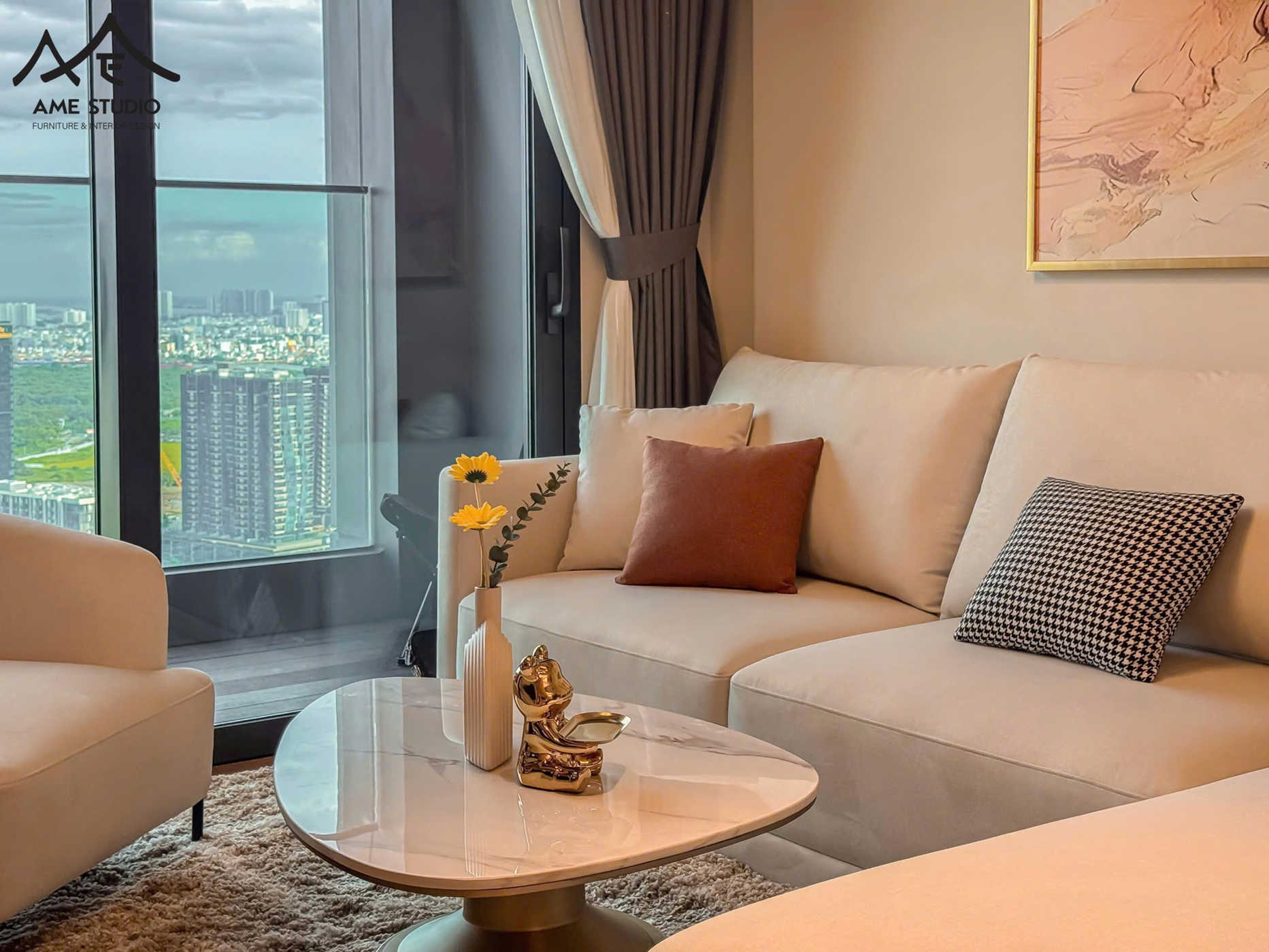 Sofa phòng khách màu kem hiện đại với bàn trà mặt đá tròn và cửa kính lớn nhìn ra thành phố