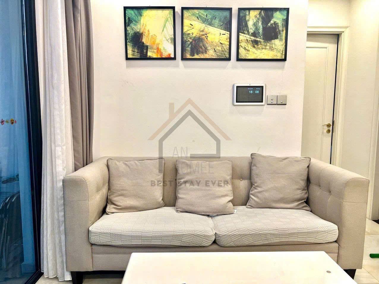 Sofa vải màu be với nhiều gối tựa trong phòng khách hiện đại treo tranh trừu tượng trên tường