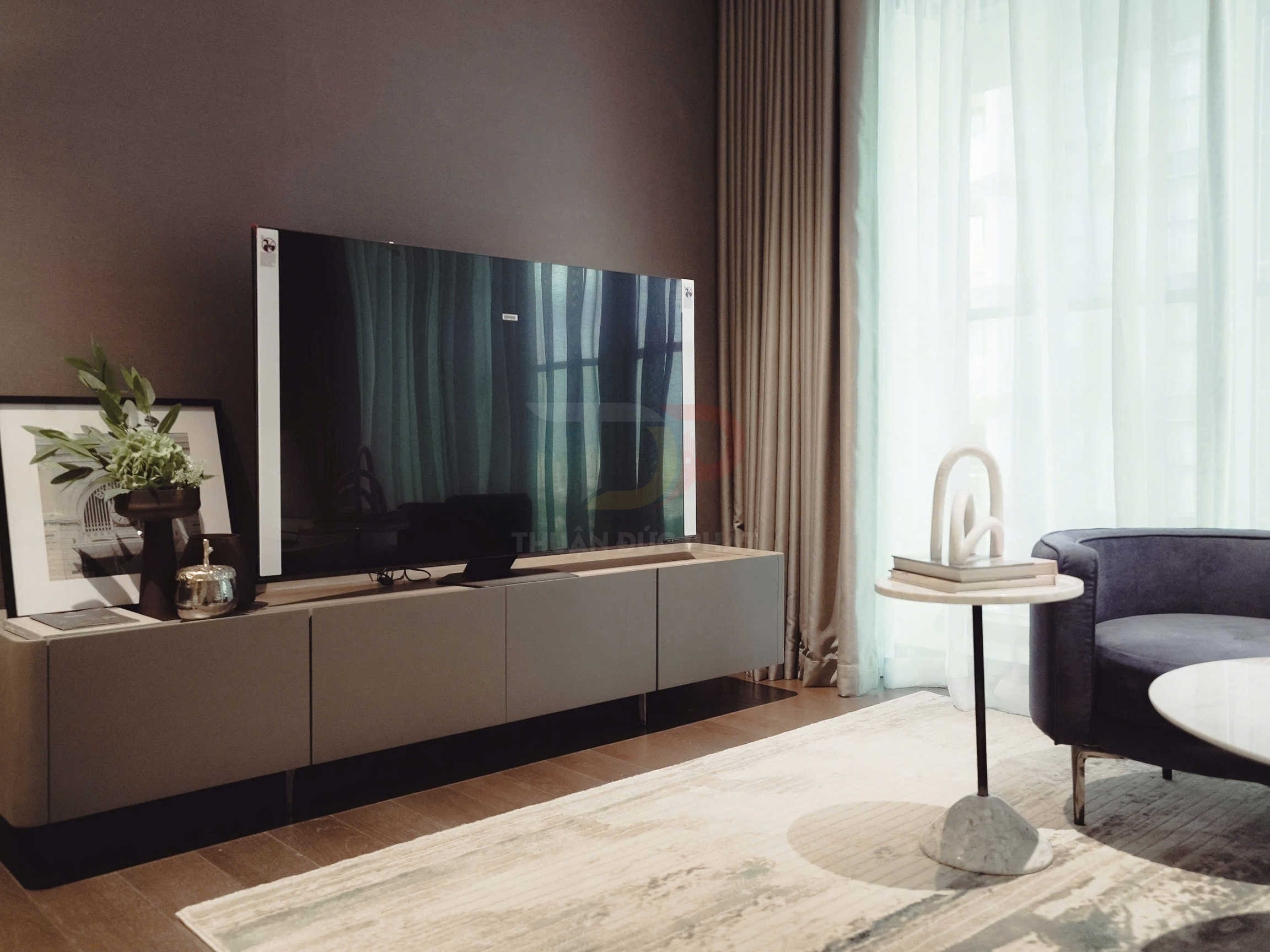 Tivi màn hình phẳng đặt trên kệ gỗ trong phòng khách hiện đại cạnh bàn trà và ghế sofa