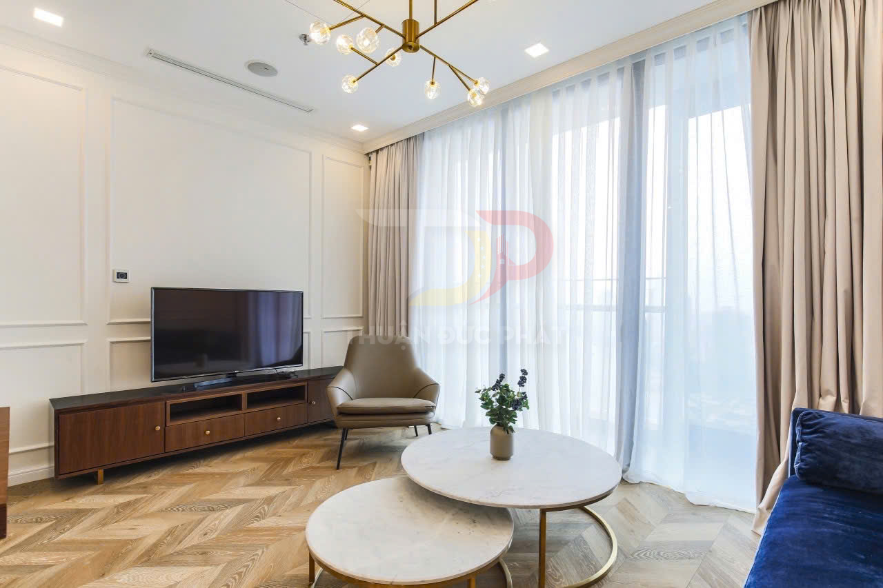 Phòng khách hiện đại với kệ tivi gỗ, tivi màn hình phẳng, bàn trà tròn đá và ghế bành cạnh cửa sổ lớn
