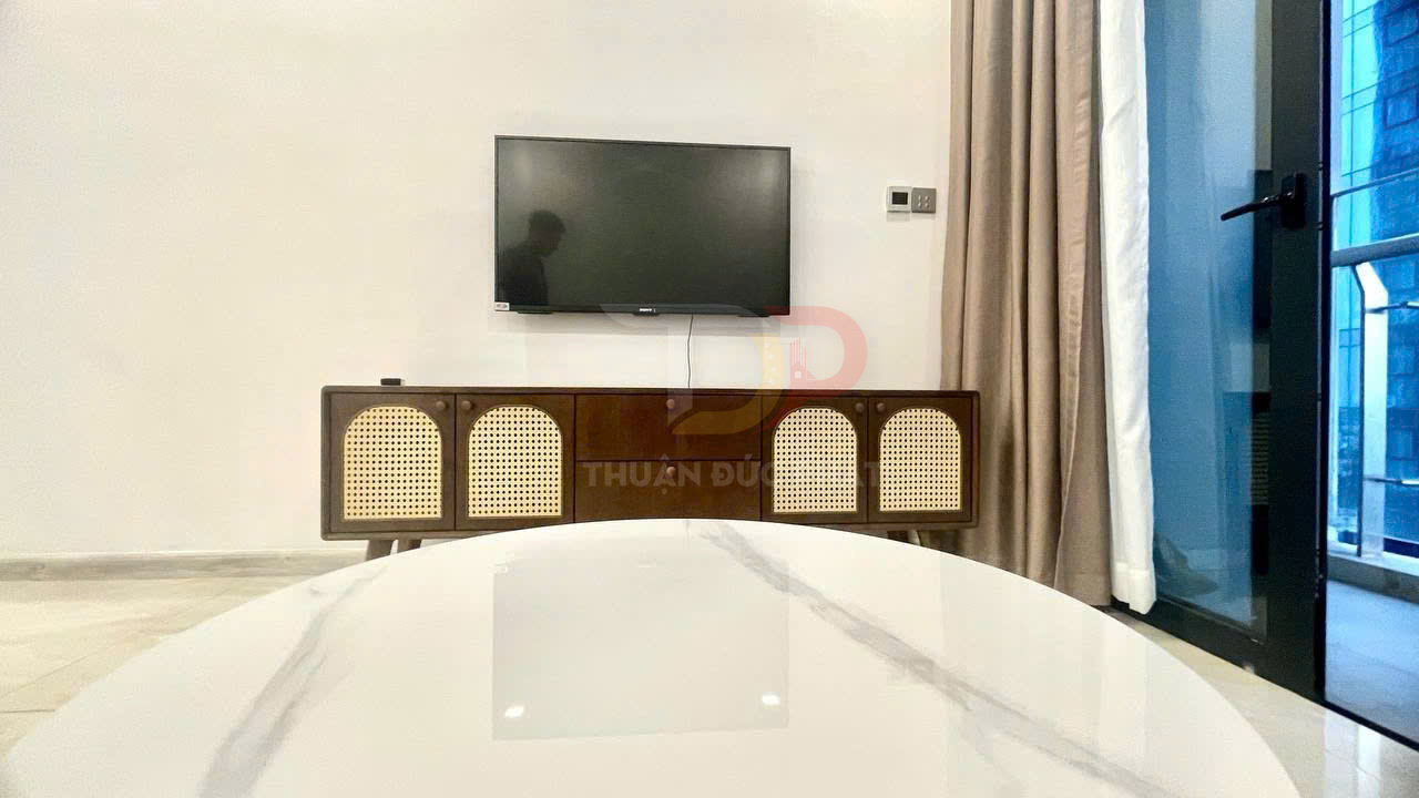 Kệ tivi gỗ mây tre hiện đại đặt dưới tivi treo tường trong phòng khách sáng rộng