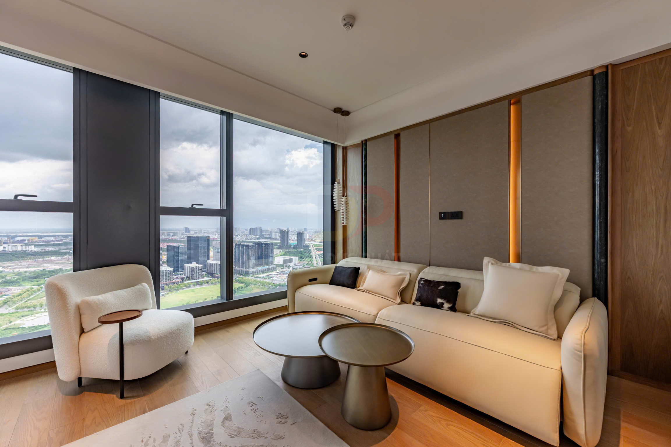 Sofa da màu kem và ghế bành vải trắng cạnh bàn trà tròn trong phòng khách view thành phố