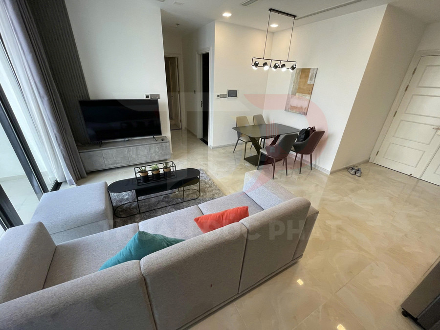 Phòng khách căn hộ hiện đại với sofa chữ L, bàn trà đen, tivi màn hình phẳng và bàn ăn bốn ghế