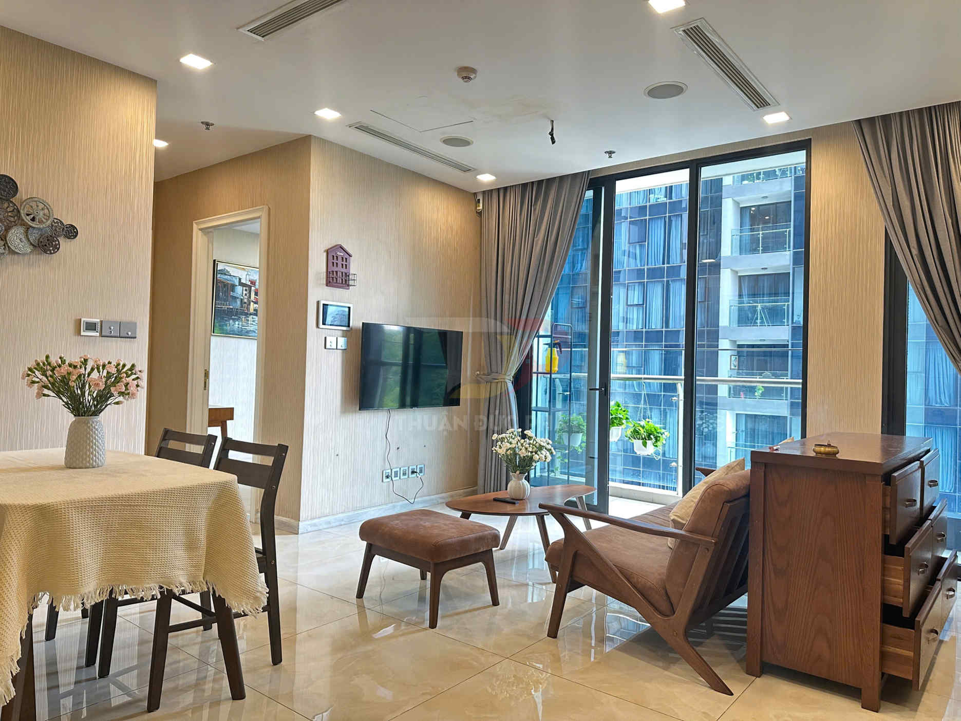 Phòng khách chung cư hiện đại với bộ bàn ghế gỗ, bàn ăn phủ khăn và cửa kính lớn nhìn ra ban công