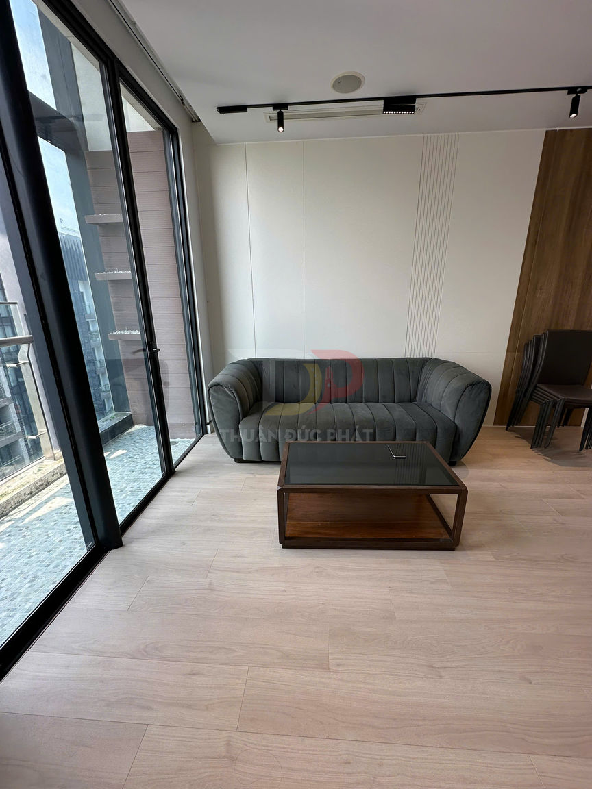 Sofa bọc nỉ màu xám và bàn trà gỗ mặt kính trong phòng khách sàn gỗ cạnh cửa kính lớn