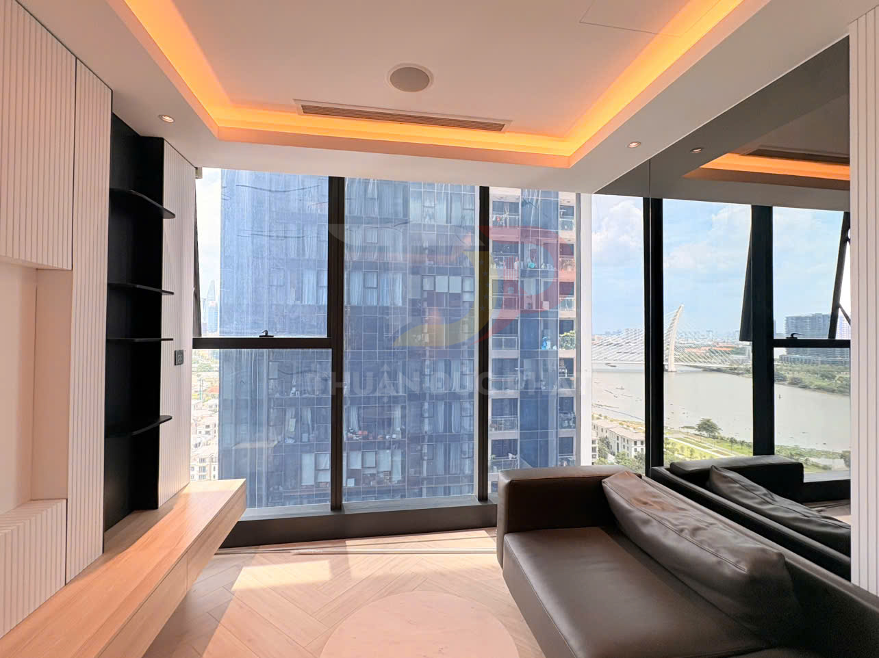 Phòng khách chung cư hiện đại với sofa da, kệ gỗ và cửa kính lớn nhìn ra sông và tòa nhà cao tầng