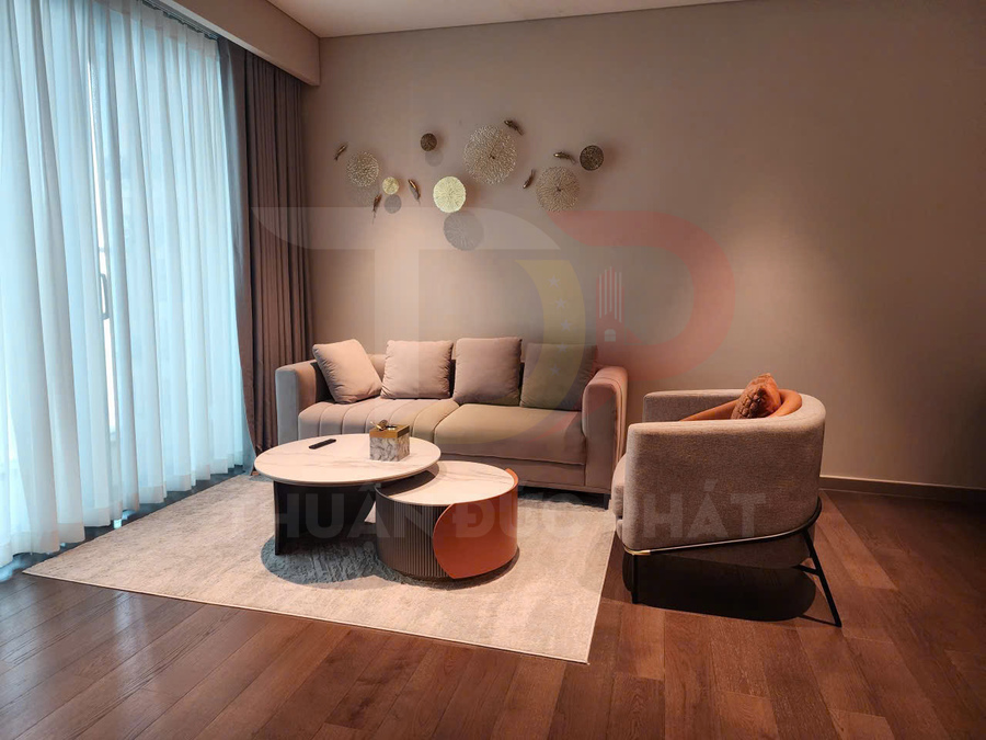 Phòng khách hiện đại với sofa chữ L màu be, ghế bành, bàn trà tròn đôi trên thảm và trang trí tường nghệ thuật