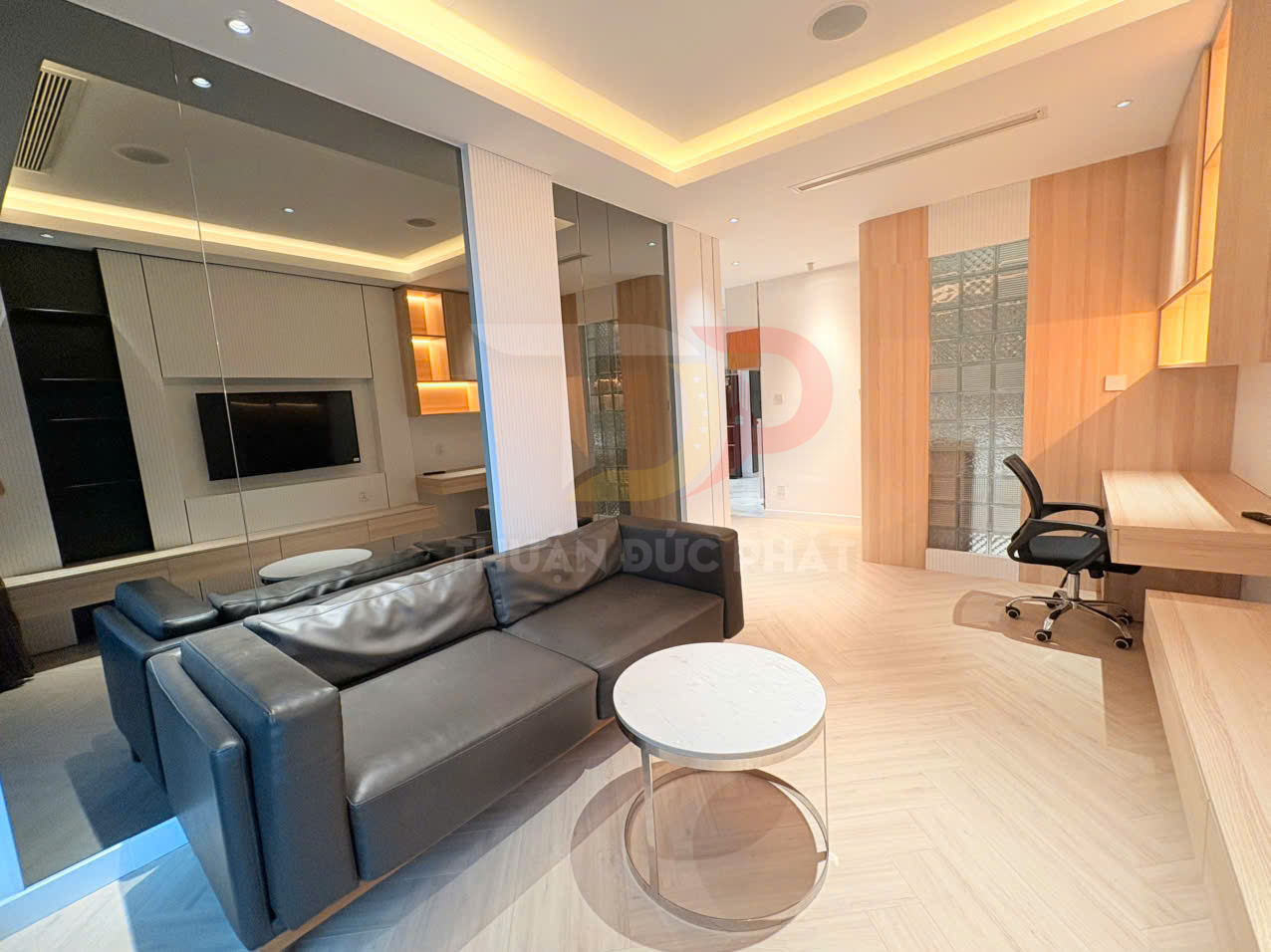 Sofa da màu đen và bàn trà tròn trong phòng khách hiện đại liền kề bàn làm việc gỗ và kệ tivi treo tường