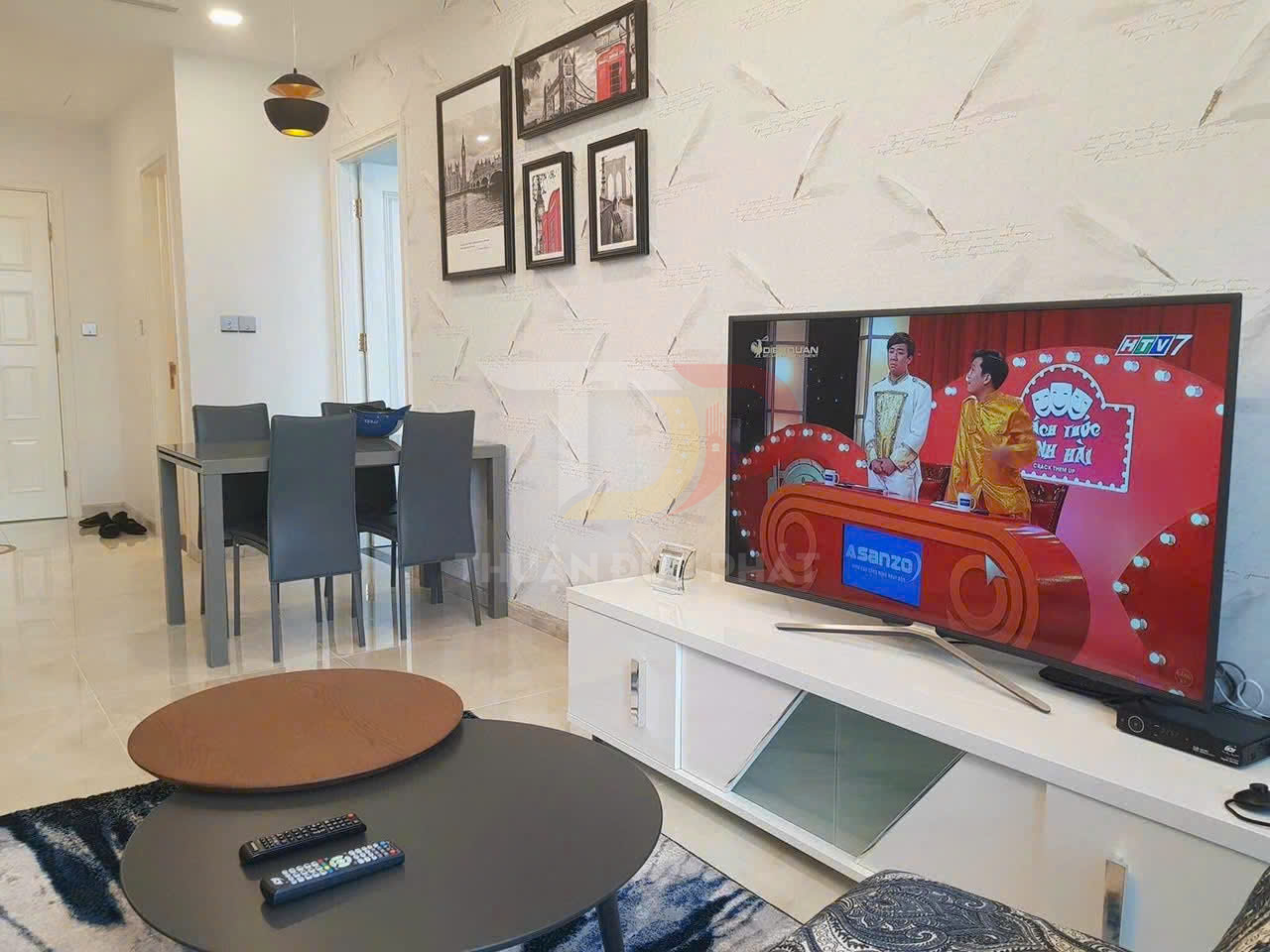 Tivi màn hình phẳng Asanzo đặt trên kệ trắng trong phòng khách hiện đại có bàn trà và bàn ăn