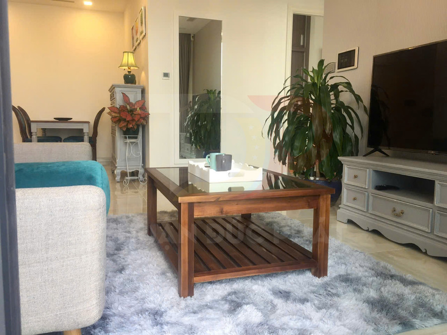 Bàn trà gỗ mặt kính đặt trên thảm lông trong phòng khách có sofa, tivi và cây xanh trang trí