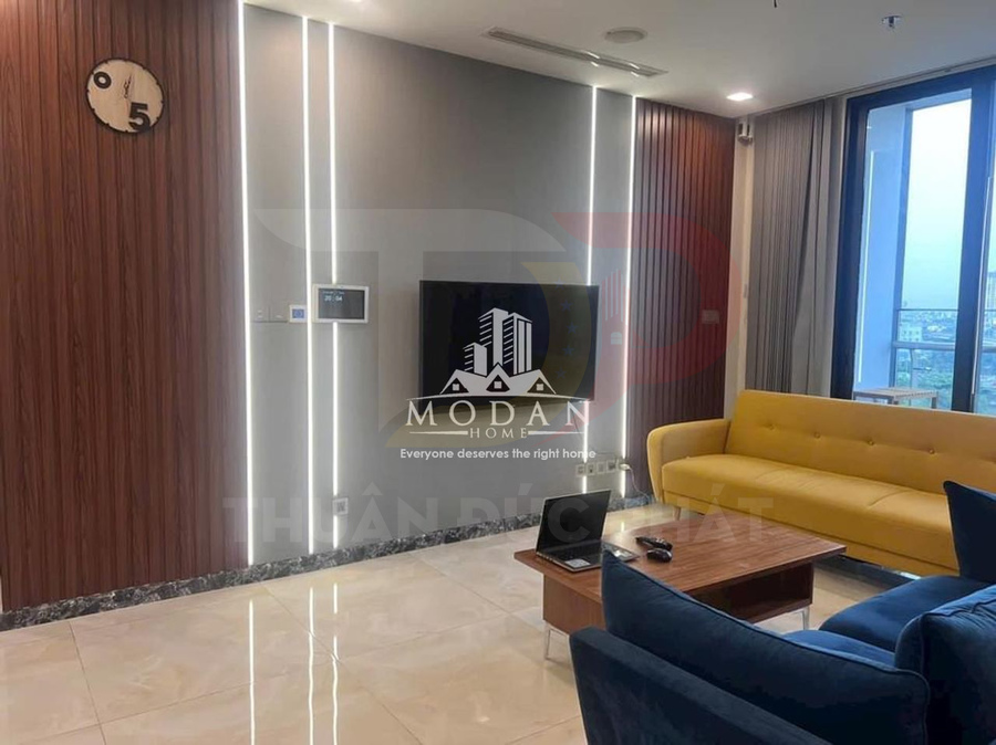 Phòng khách chung cư hiện đại với sofa vàng, bàn gỗ nhỏ và tivi treo tường cạnh cửa sổ lớn