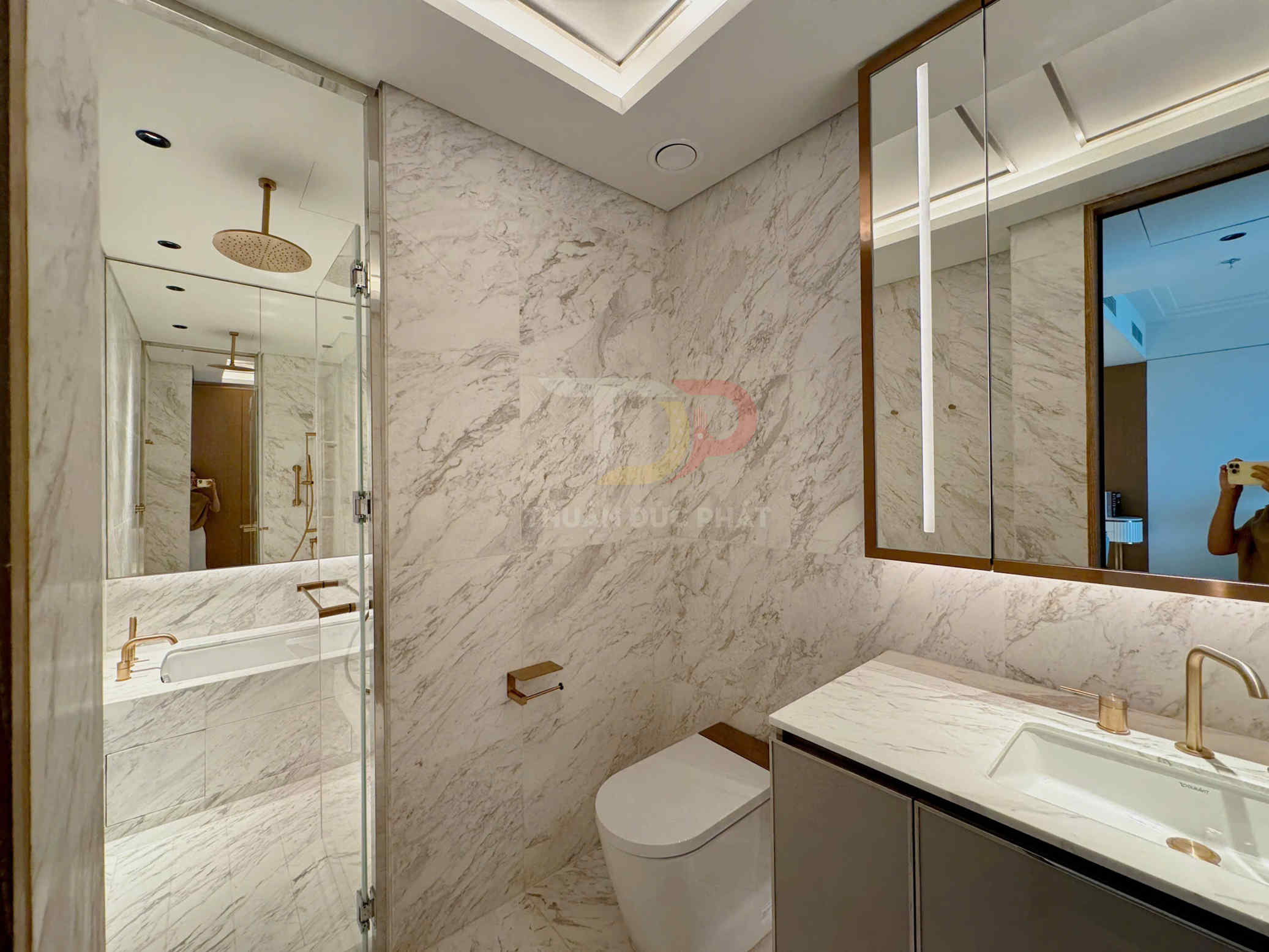 Phòng tắm cao cấp ốp đá marble với bồn tắm kính, lavabo và vòi nước màu vàng đồng sang trọng
