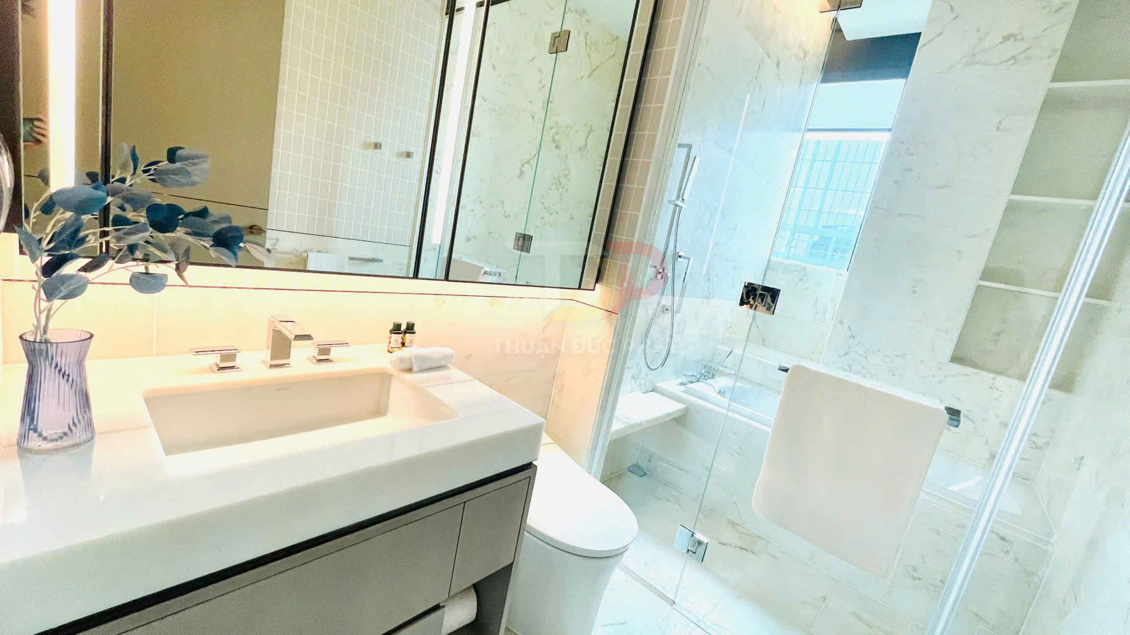 Phòng tắm hiện đại với bồn rửa mặt đá trắng, vòi nước inox, buồng tắm kính và phụ kiện vệ sinh cao cấp
