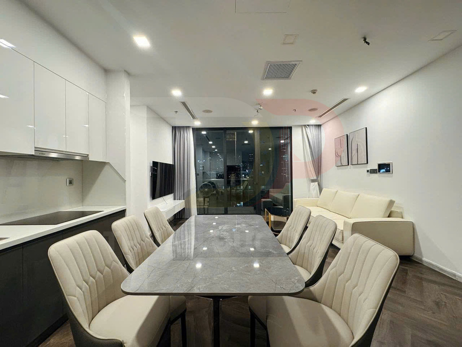 Bàn ăn mặt đá với sáu ghế bọc da trong căn hộ hiện đại liền kề bếp và phòng khách sáng đèn