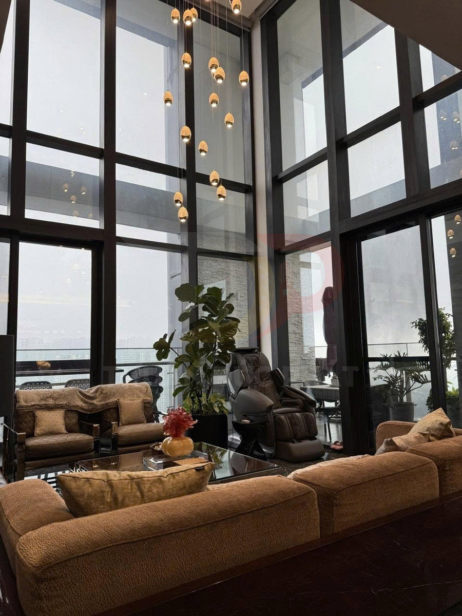 Ghế massage toàn thân trong phòng khách sang trọng với sofa nâu, cửa kính lớn và đèn thả trần hiện đại