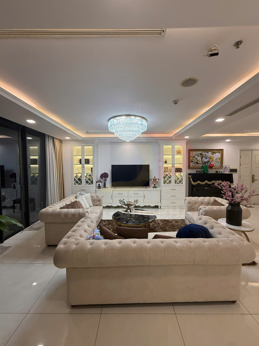 Phòng khách sang trọng với bộ sofa bọc nỉ màu kem, bàn trà đá tròn và kệ tivi trắng hiện đại