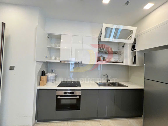 Tủ bếp hiện đại màu trắng xám với bếp từ, lò nướng âm tủ và chậu rửa inox trong căn hộ nhỏ