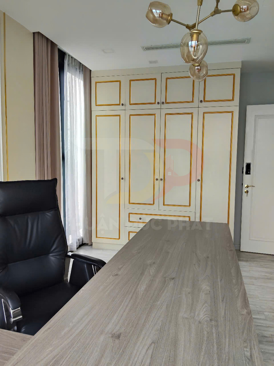 Bàn làm việc gỗ hiện đại với ghế da đen và tủ âm tường cửa trắng viền vàng trong phòng làm việc sáng