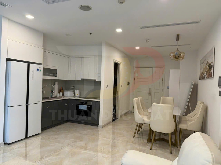 Phòng bếp và bàn ăn hiện đại với tủ bếp chữ L, tủ lạnh lớn và bộ bàn ghế da màu kem