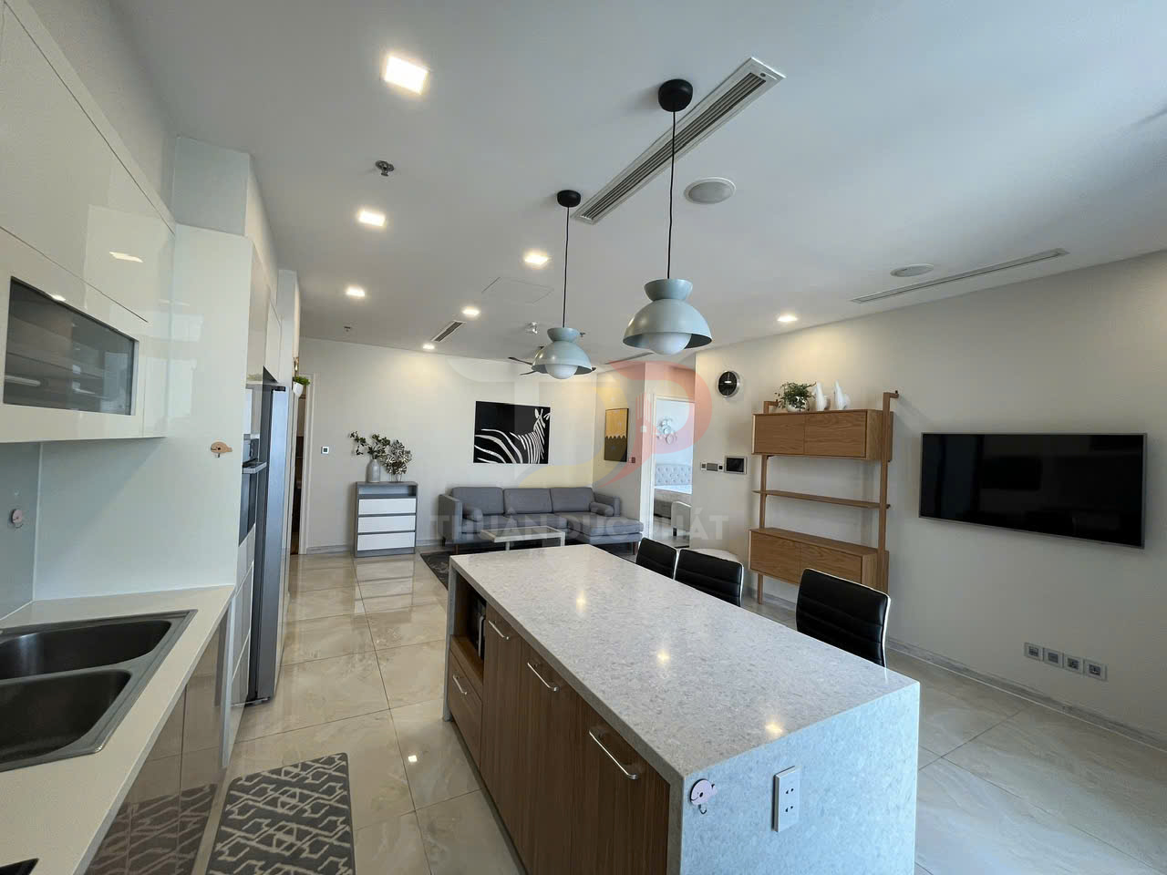 Căn hộ hiện đại với bếp đảo, tủ bếp trắng, sofa xám và kệ gỗ cạnh tivi treo tường
