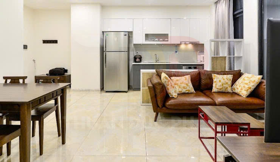 Phòng khách căn hộ với sofa da nâu, bàn gỗ và bếp tích hợp tủ lạnh inox hiện đại