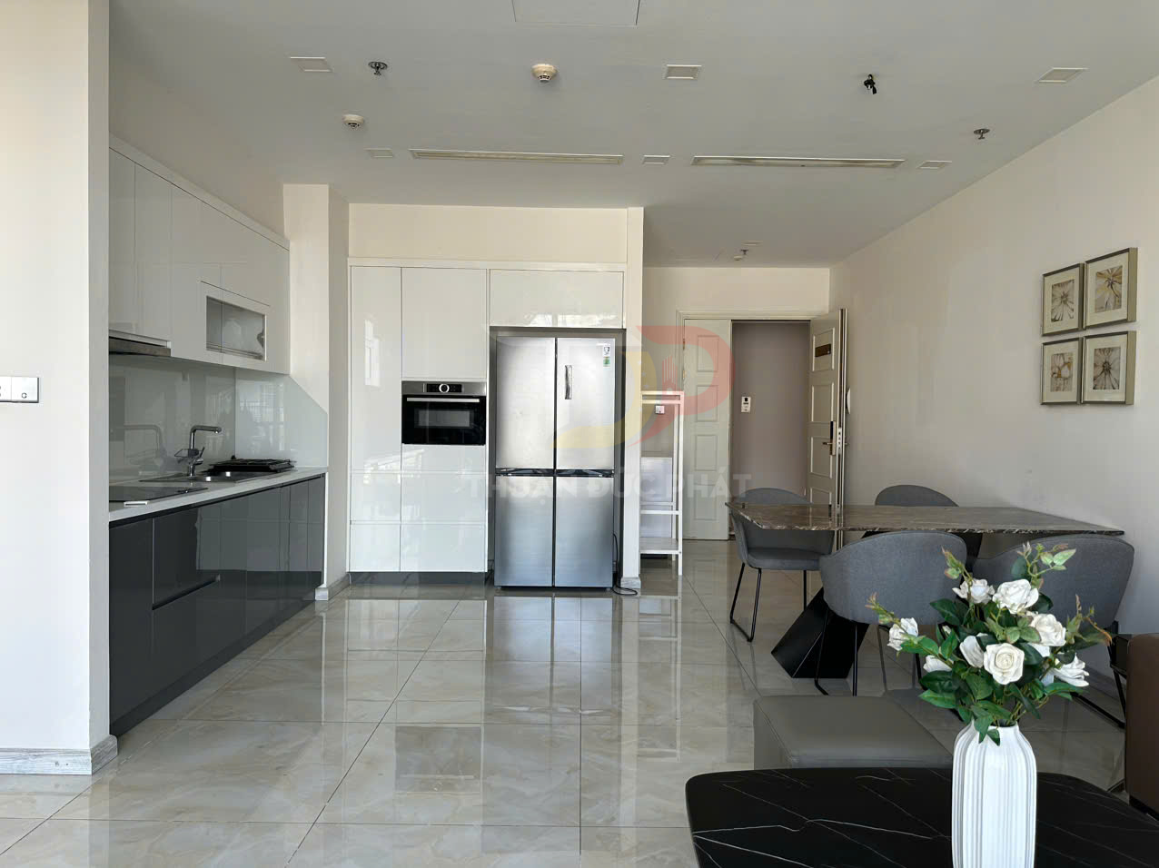 Bếp và phòng ăn hiện đại với tủ bếp âm tường, tủ lạnh inox lớn và bàn ăn ghế nệm xám