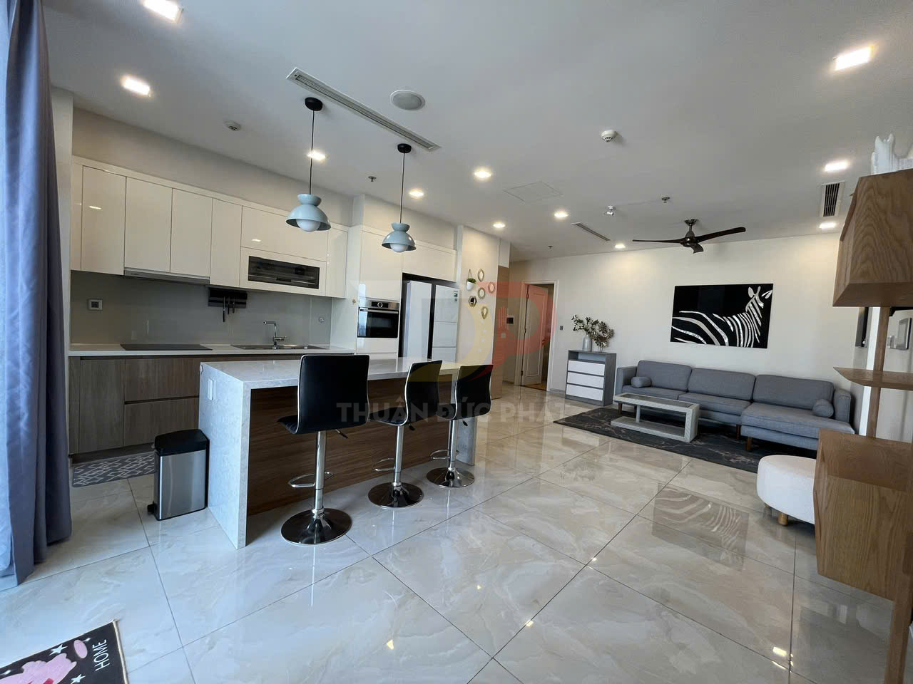Phòng khách liền bếp hiện đại với đảo bếp, ghế bar da đen và sofa xám trong căn hộ cao cấp