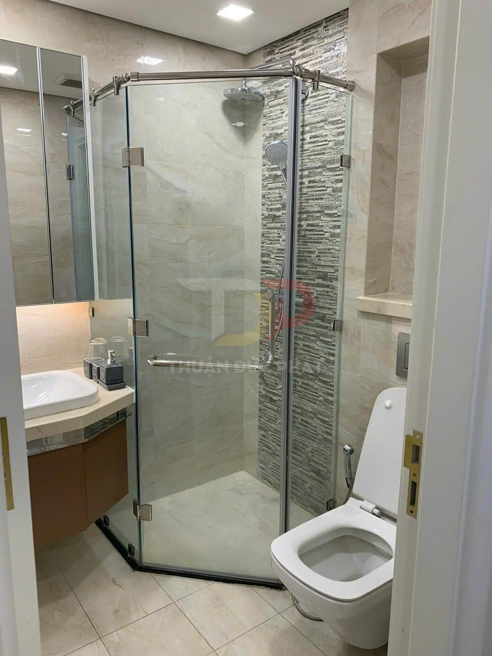 Phòng tắm hiện đại với buồng tắm kính, vòi sen treo tường, bồn rửa và bồn cầu sứ trắng