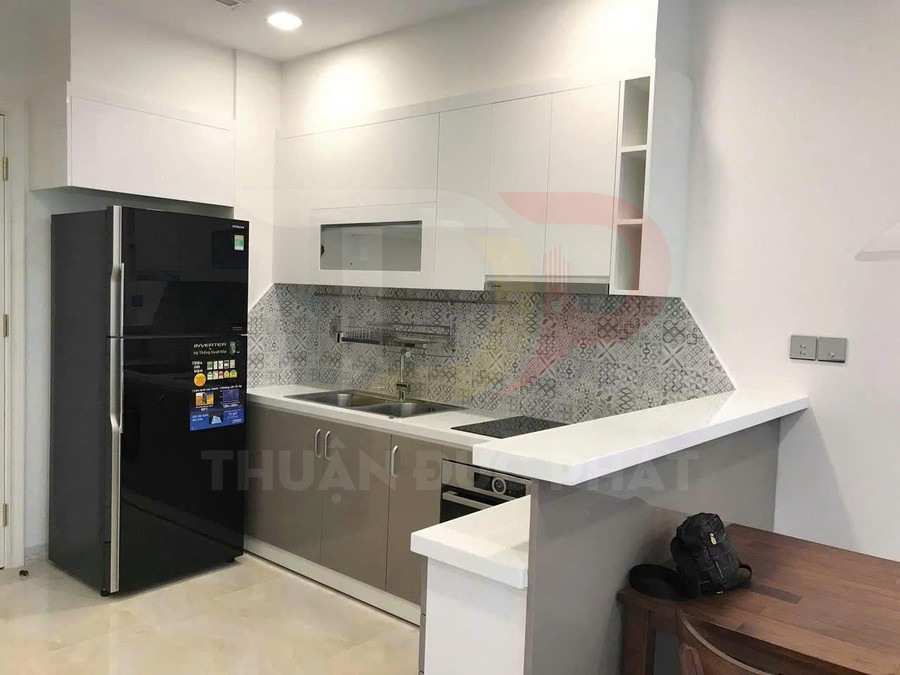 Tủ bếp chữ L hiện đại với tủ lạnh đen, bồn rửa inox, bếp điện âm và mặt bàn đá trắng