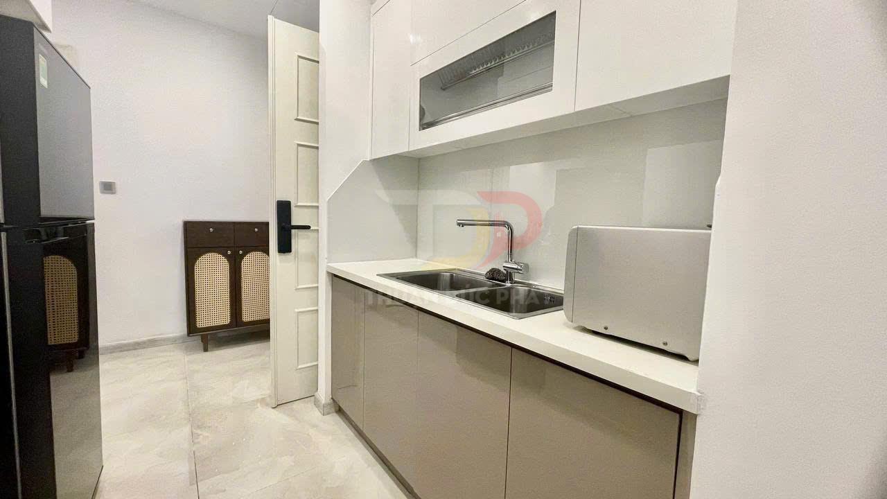 Bếp nhỏ hiện đại với tủ bếp trắng, bồn rửa inox, lò vi sóng và tủ lạnh hai cửa màu đen