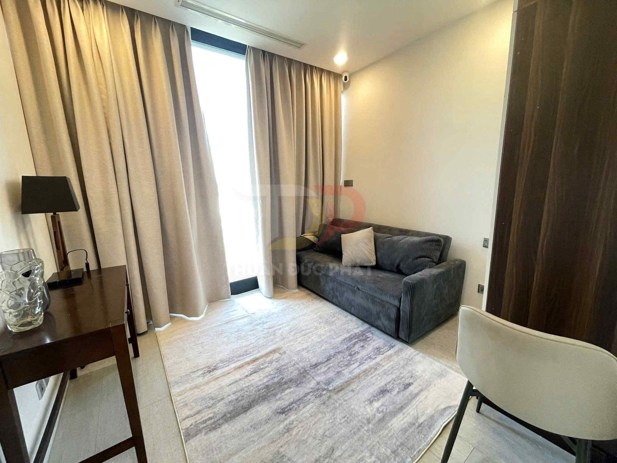 Phòng khách nhỏ với sofa vải xám, bàn gỗ và rèm cửa màu be sáng