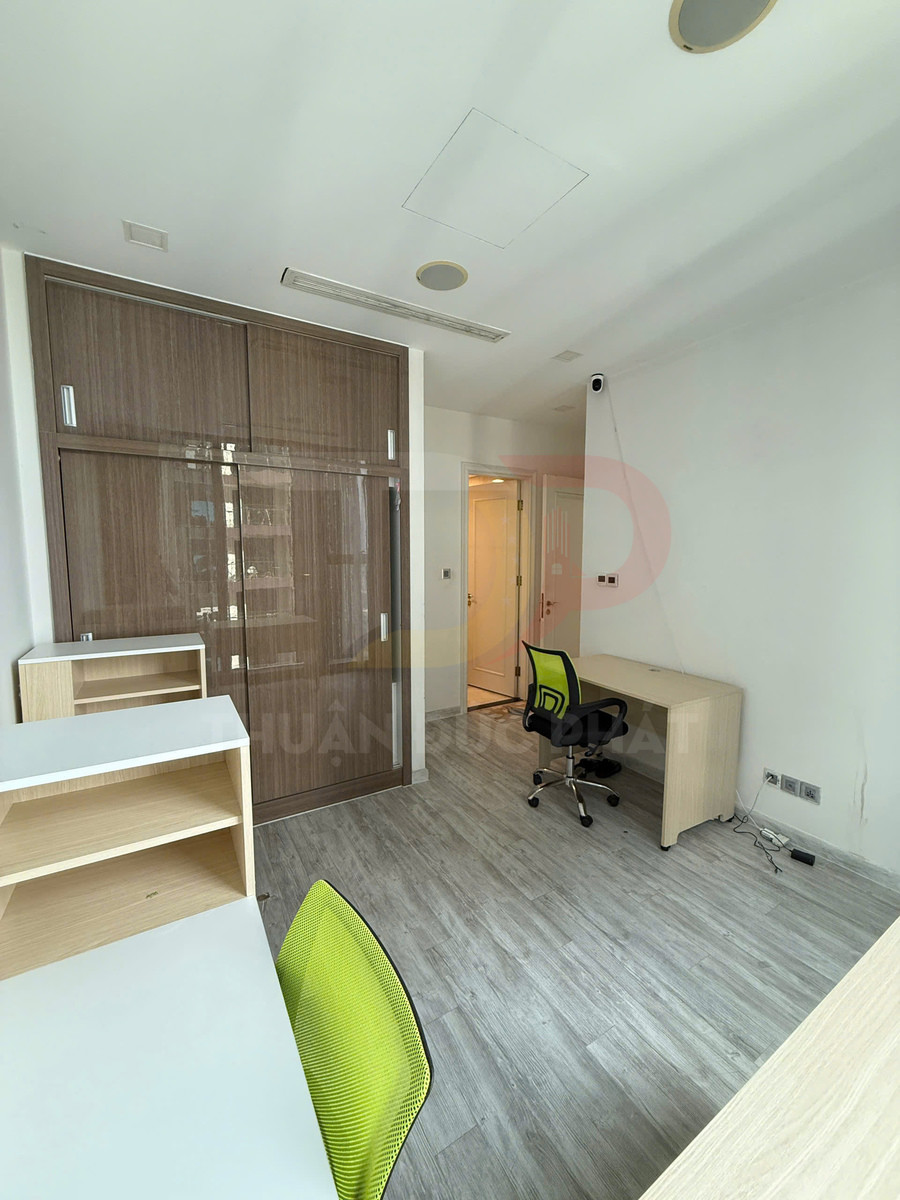Phòng làm việc nhỏ với bàn gỗ, ghế xoay lưới màu xanh và tủ gỗ cửa trượt hiện đại