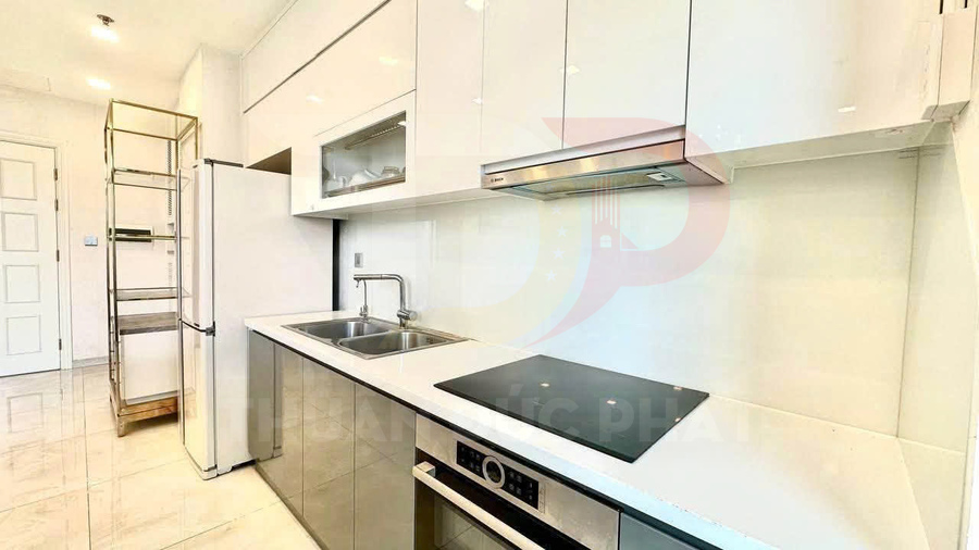Bếp hiện đại với tủ bếp trắng, bếp từ âm, máy hút mùi và chậu rửa inox trong căn hộ sáng sủa