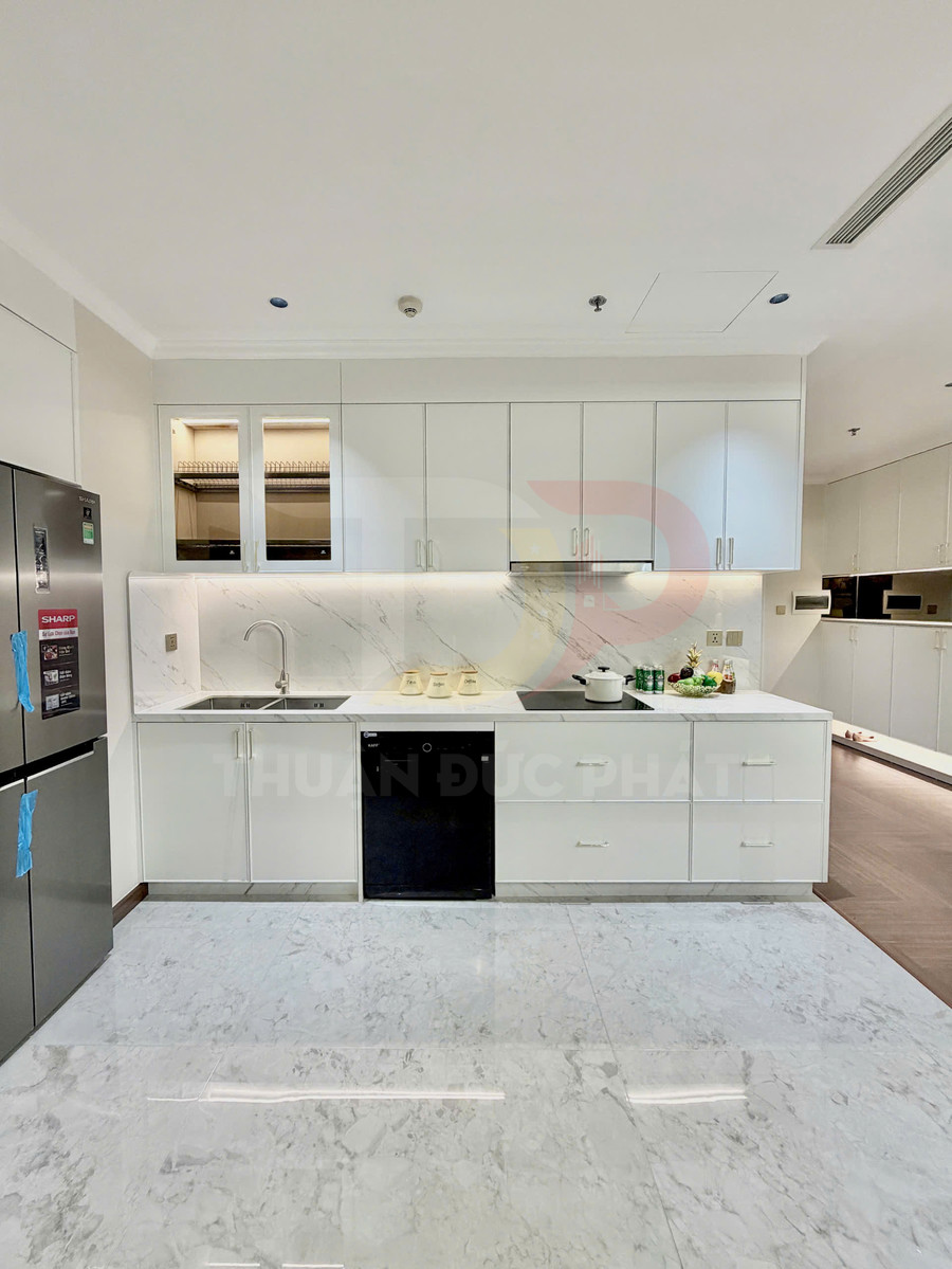Tủ bếp nhựa cao cấp màu trắng với mặt đá vân mây, bếp từ và chậu rửa inox hiện đại trong căn hộ cao cấp