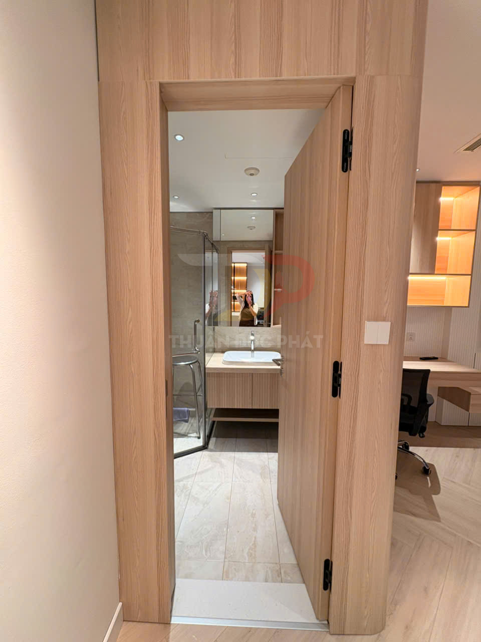 Cửa gỗ phòng tắm mở vào không gian nội thất hiện đại với buồng tắm kính và lavabo
