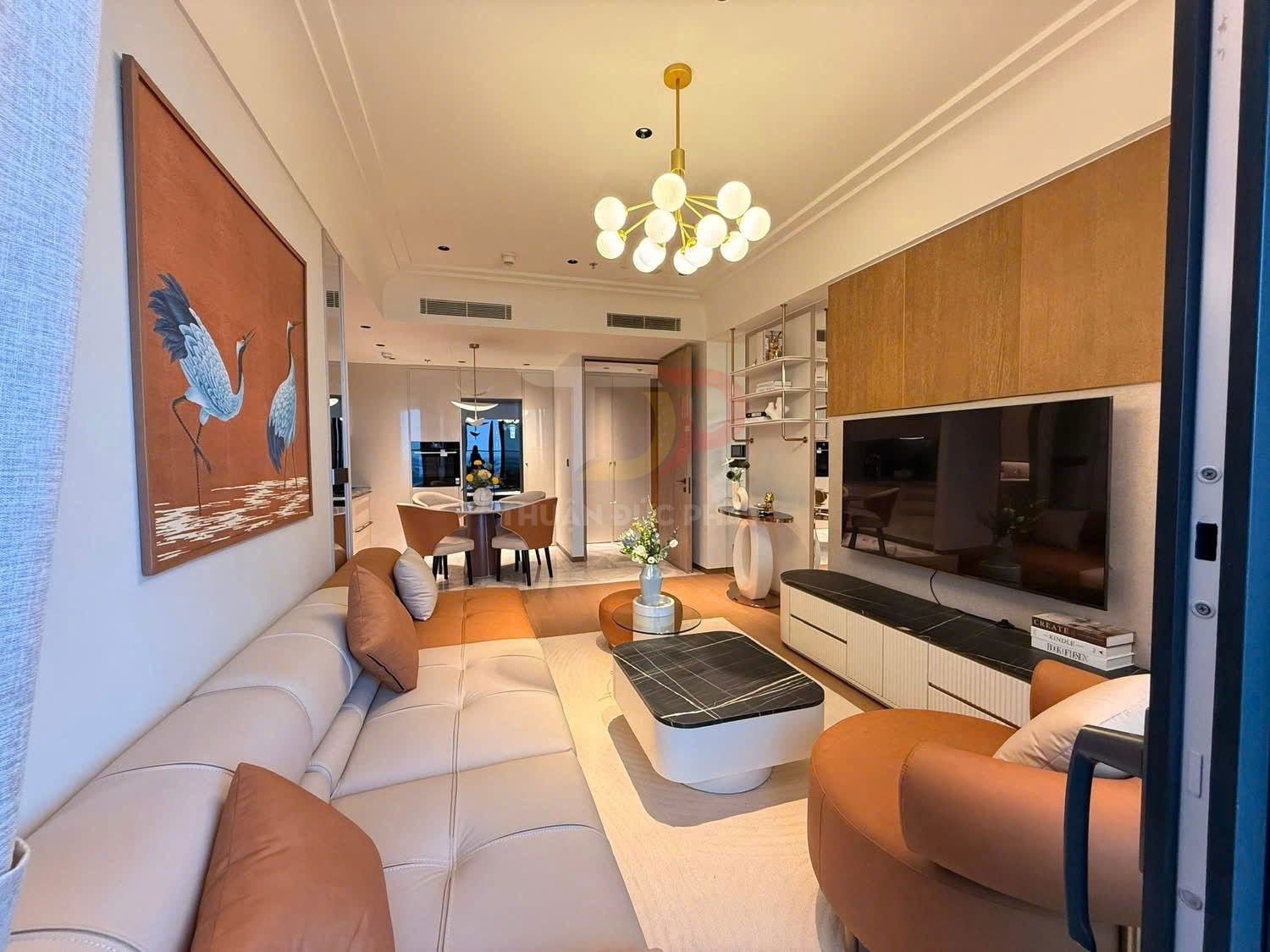 Phòng khách chung cư hiện đại với sofa da, bàn trà, kệ tivi lớn và tranh treo tường tông cam trang trí