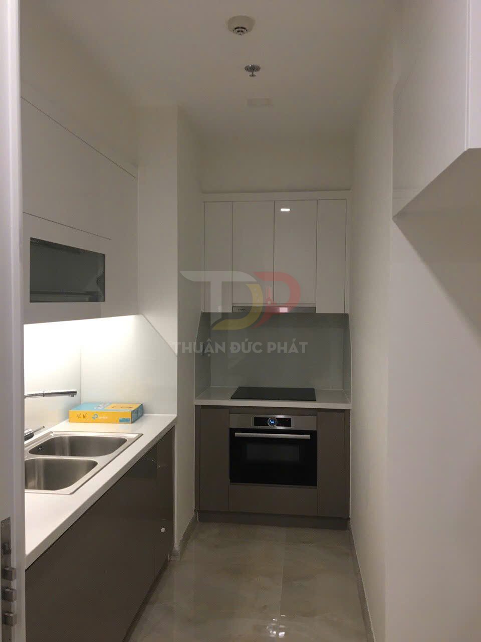 Bếp nhỏ hiện đại với tủ bếp âm tường, bồn rửa đôi inox và bếp từ kèm lò nướng âm tủ