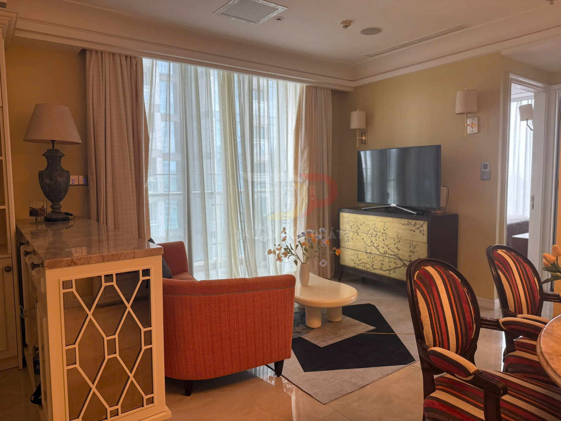 Phòng khách chung cư cao cấp với sofa cam, bàn trà nhỏ, tivi màn hình phẳng trên kệ gỗ hoa văn