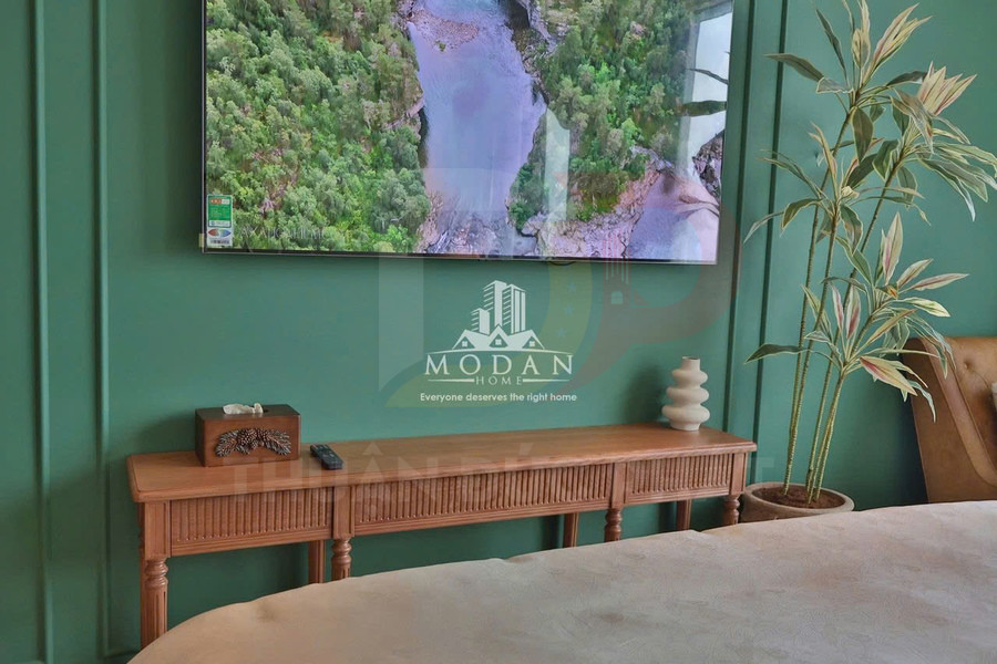 Kệ gỗ trang trí dưới tivi treo tường trong phòng ngủ màu xanh, đặt chậu cây và đồ decor hiện đại