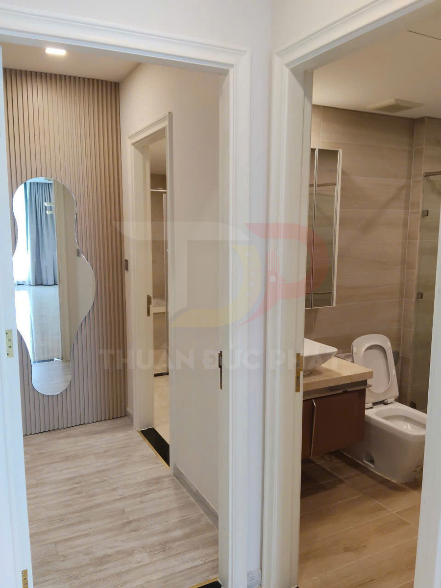 Hành lang căn hộ với cửa vào phòng tắm hiện đại, bồn cầu và lavabo, sàn gỗ sáng màu