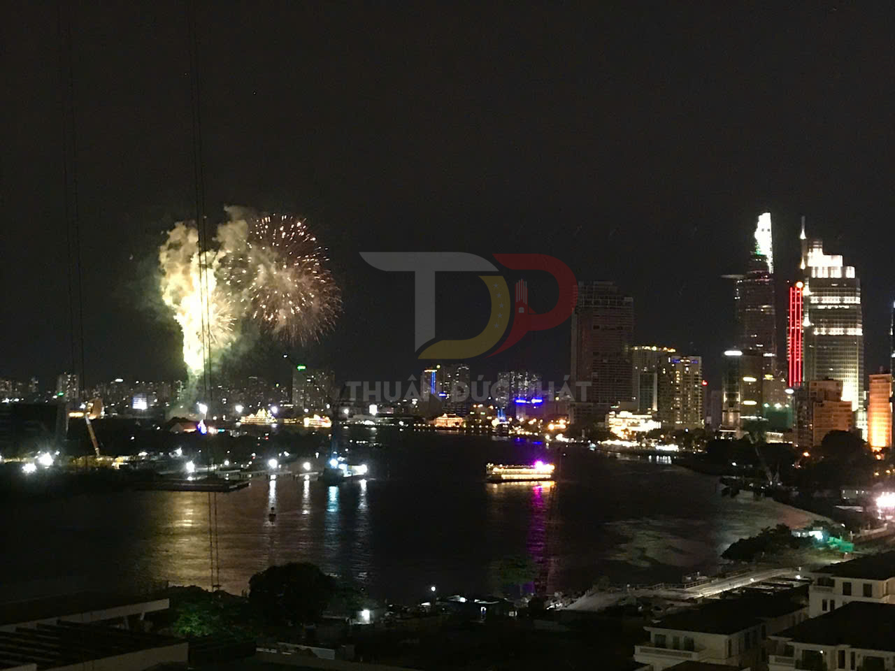 Pháo hoa rực sáng trên bầu trời đêm bên sông và khu trung tâm thành phố hiện đại