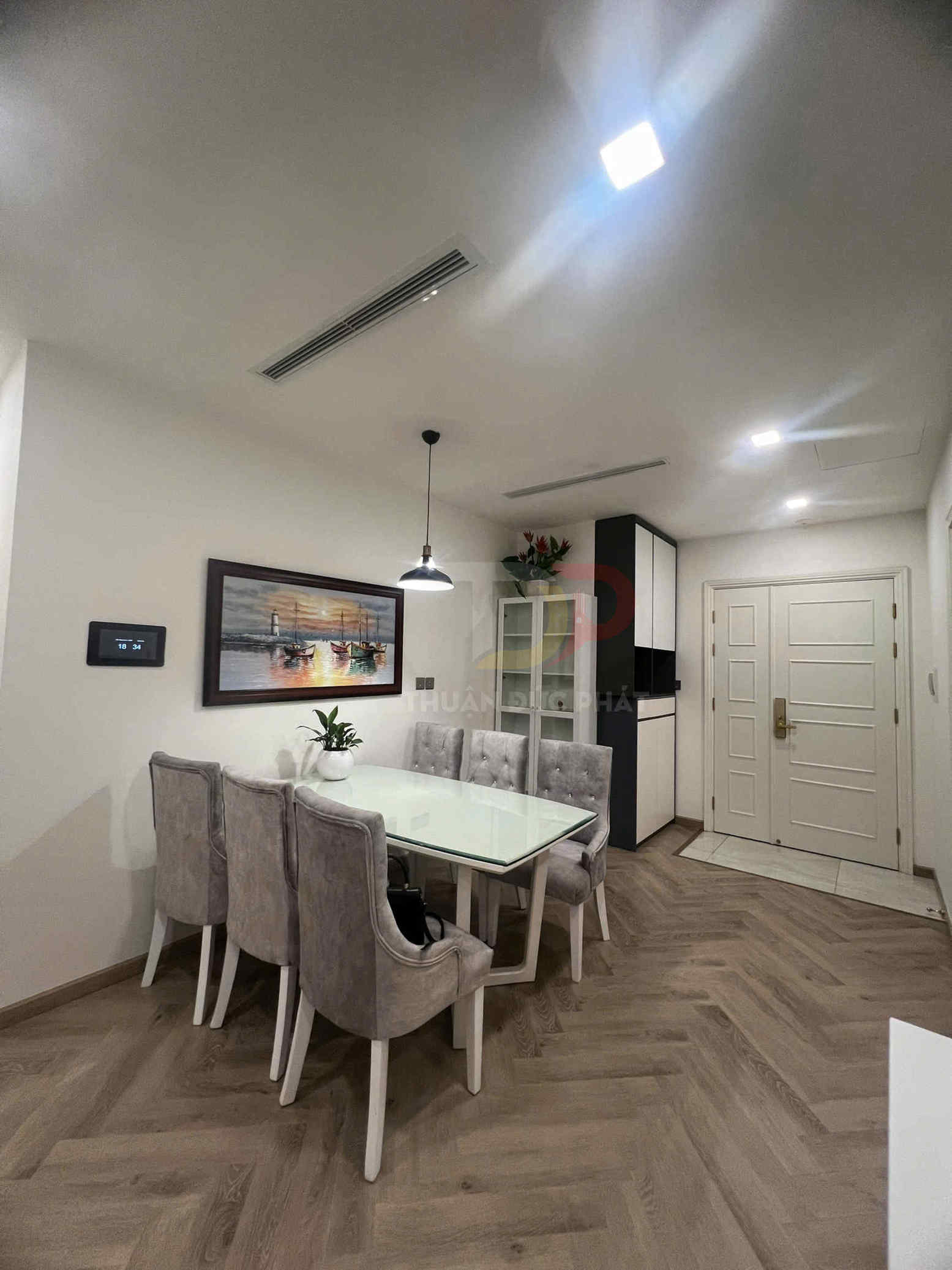 Bộ bàn ăn mặt kính với sáu ghế bọc nỉ màu xám trong phòng ăn chung cư hiện đại