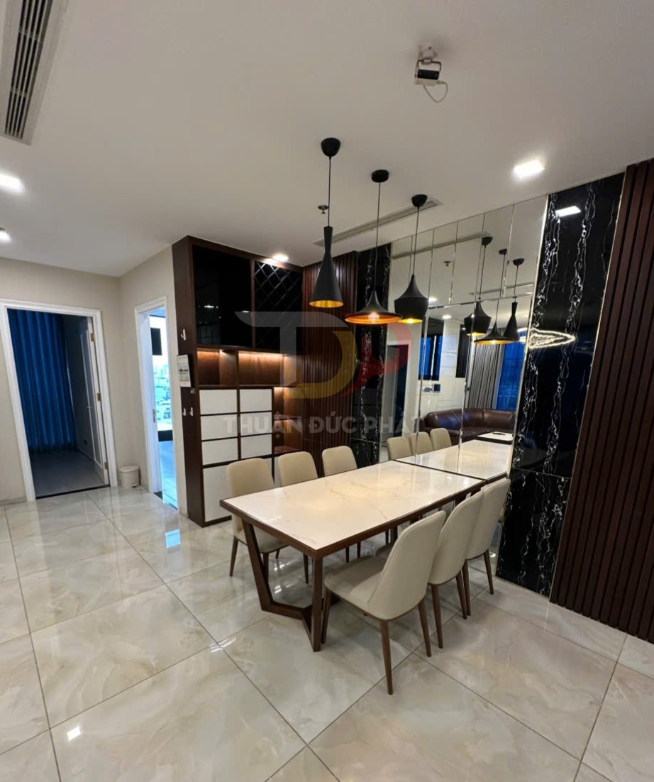 Bàn ăn mặt đá chữ nhật với tám ghế nệm da màu kem trong phòng ăn chung cư hiện đại